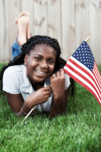 african american teen with braces smiling in the grass holding an American flag